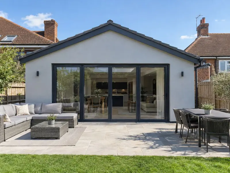 A single-storey rear extension in pale grey acrylic render with large black bifold doors and a patio