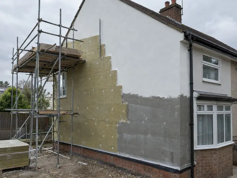 Side gable of a semi-detached house part-way through external wall insulation, with mineral wool slabs, mesh base coat and finished white render