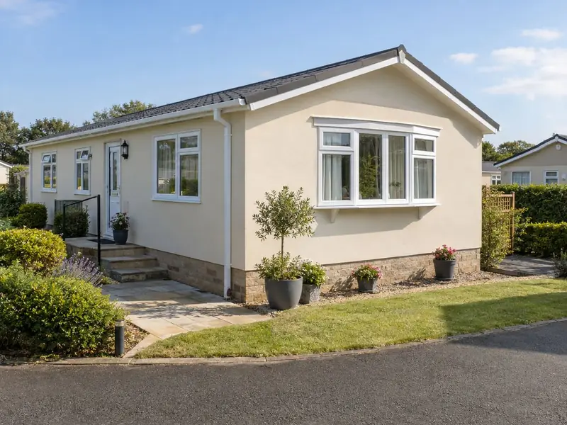 A single-storey park home finished in smooth stone-coloured render with a small planted garden